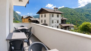 Un balcon doté d’un espace salon extérieur, offrant une vue sur un paysage montagneux parsemé de bâtiments traditionnels.