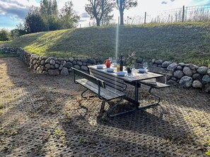 Une table de pique-nique installée à l’extérieur, avec des murs en pierre et une colline verdoyante en arrière-plan.