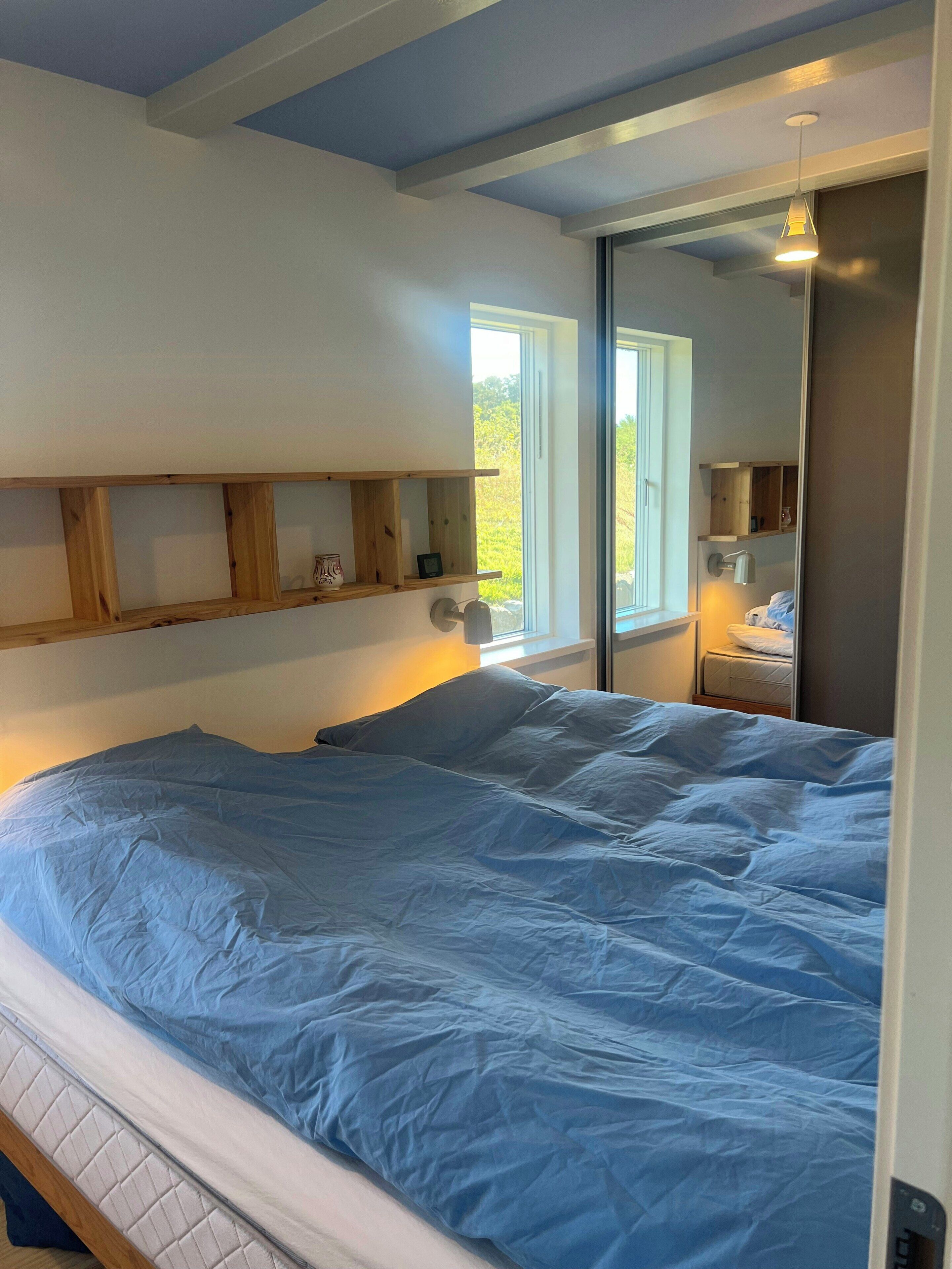 A bedroom with a bed, wooden headboard, bedside tables, a window, and a nightstand.