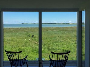 Ein Zimmer mit zwei Sesseln vor einem großen Fenster mit Blick auf ein grasbewachsenes Feld und ein Gewässer.