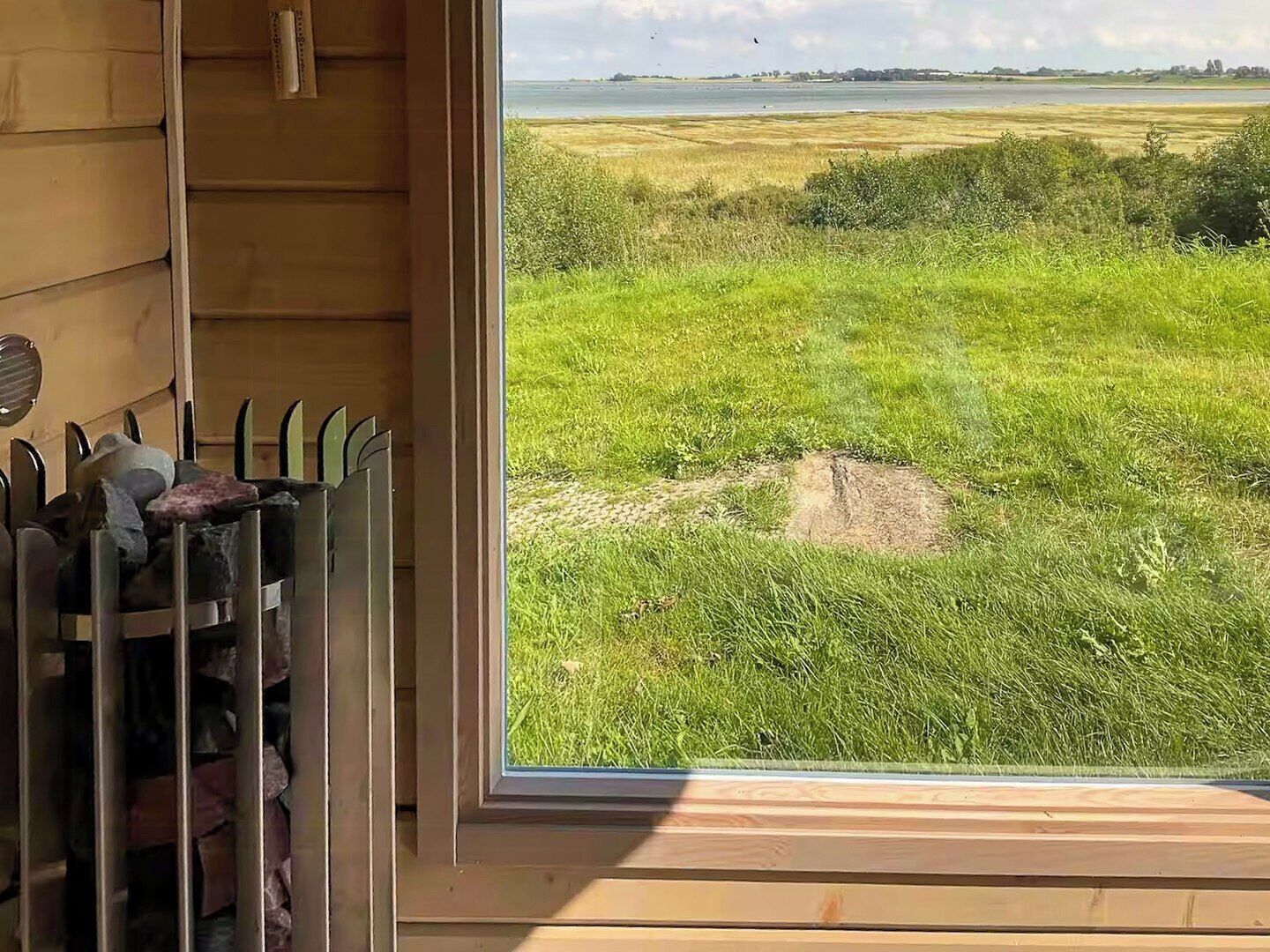 Una habitación con un amplio ventanal que da a un campo cubierto de hierba y un cuerpo de agua.