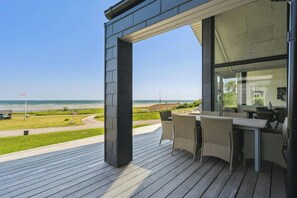 Una terraza moderna al aire libre con vista a la playa, mobiliario de mimbre y cielo despejado.