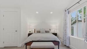 Une chambre à coucher comprenant un lit, un banc, des tables de chevet, des lampes et une fenêtre avec des rideaux.