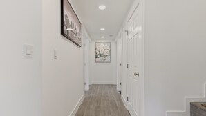 Un couloir avec un plancher en bois, des murs blancs et un tableau encadré sur le côté gauche.