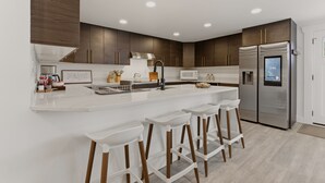 Une cuisine moderne dotée d’un îlot central, d’appareils électroménagers en acier inoxydable et de tabourets de bar en bois.