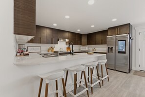 A modern kitchen with a central island, stainless steel appliances, and wooden bar stools. - Spacious 5BR Home Near Seattle & SeaTac - Parking (Burien)