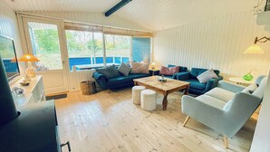 A living room with a sofa, armchair, coffee table, and a view of the outdoors. - Cottage near forest and beach (Glesborg)