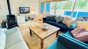 A living room with a sofa, a coffee table, a TV, and a fireplace. - Cottage near forest and beach (Glesborg)