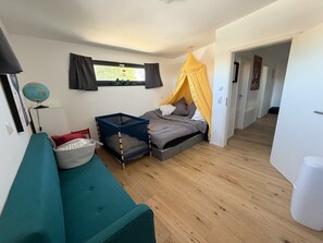 Ein Schlafzimmer mit einem Bett, einer blauen Kommode, einem grünen Sofa, einem Globus auf einem Tisch und einem Fenster mit Vorhängen.