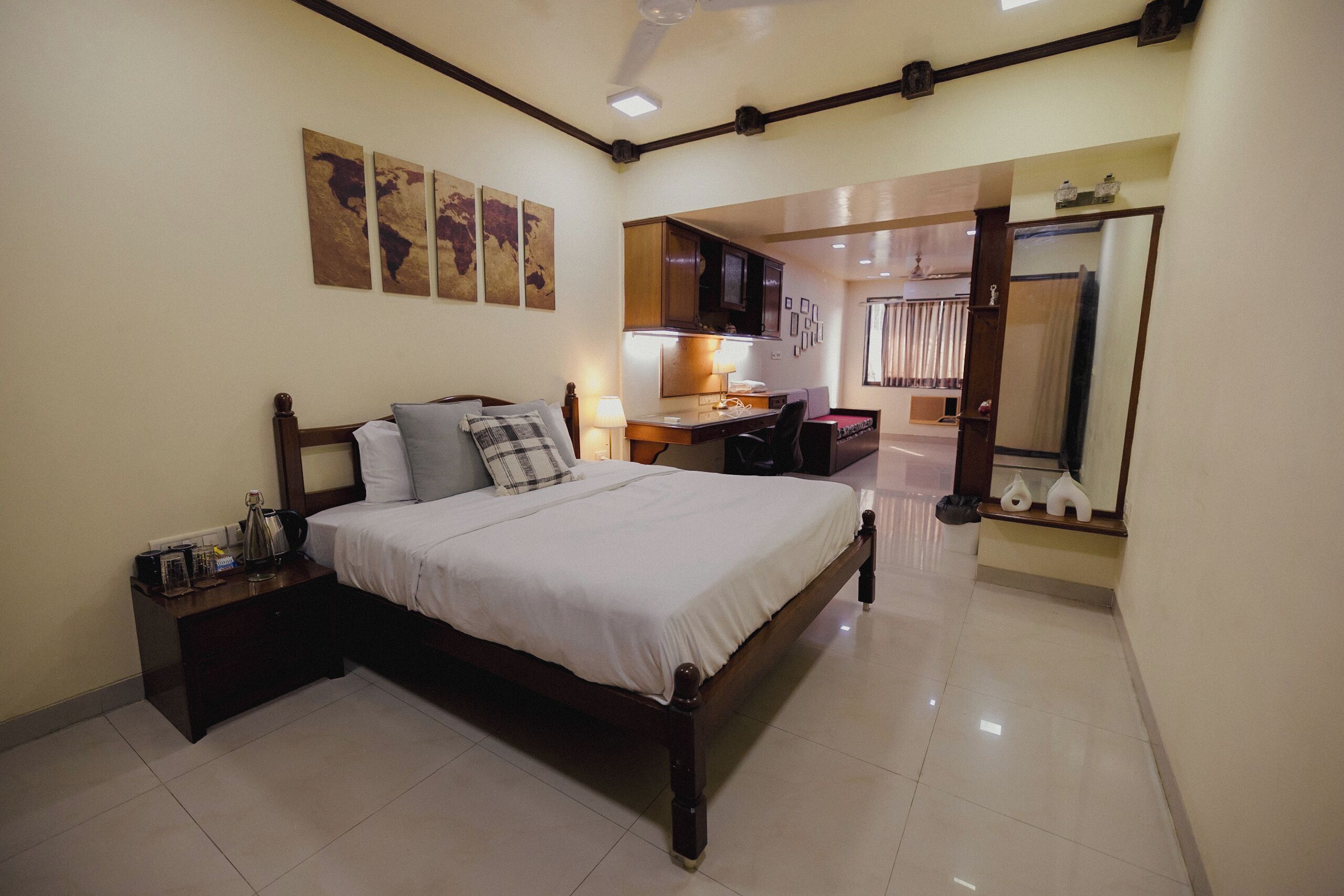 A bedroom with a bed, bedside table, lamp, and a view into the kitchen.