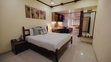 A bedroom with a bed, bedside table, lamp, and a view into the kitchen.