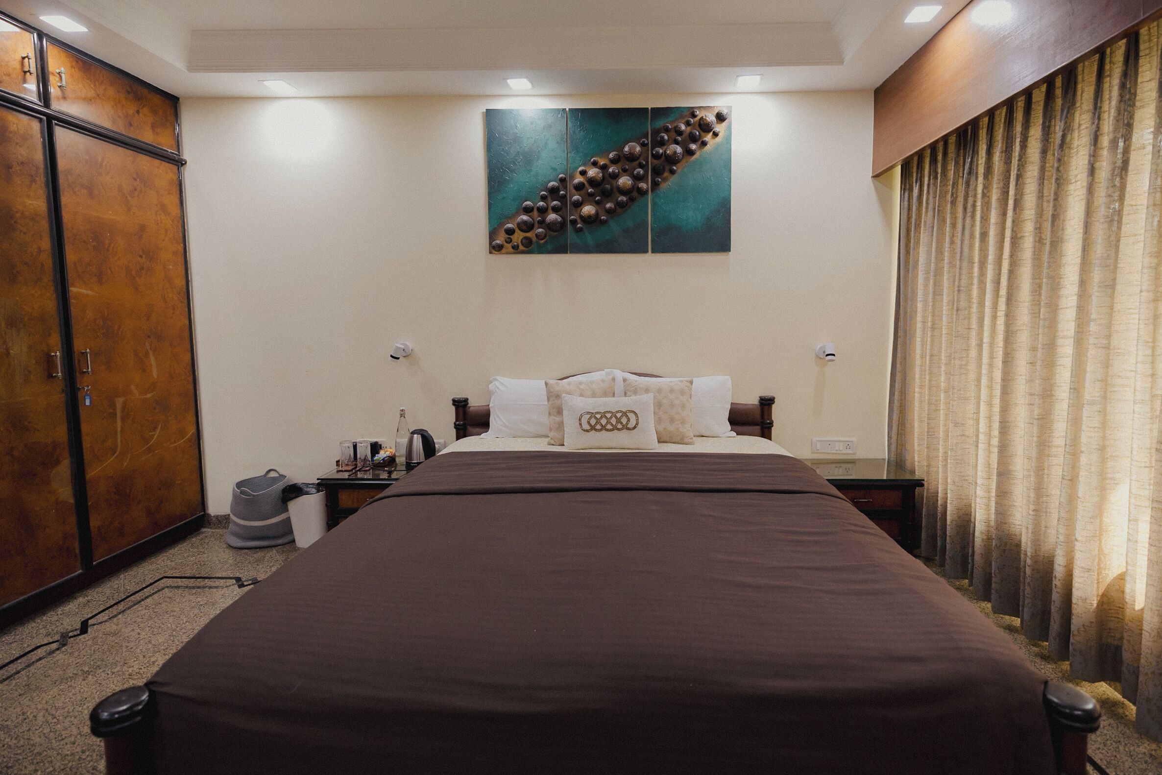 Quarto de hotel com uma cama grande, um guarda-roupa, um quadro na parede e uma cortina na janela.