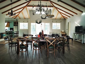 A spacious dining area with wooden chairs and a large table, a kitchen in the background, and a high ceiling with exposed beams. - KhaoYai 6 Bedrooms pool villa (Khanong Phra)