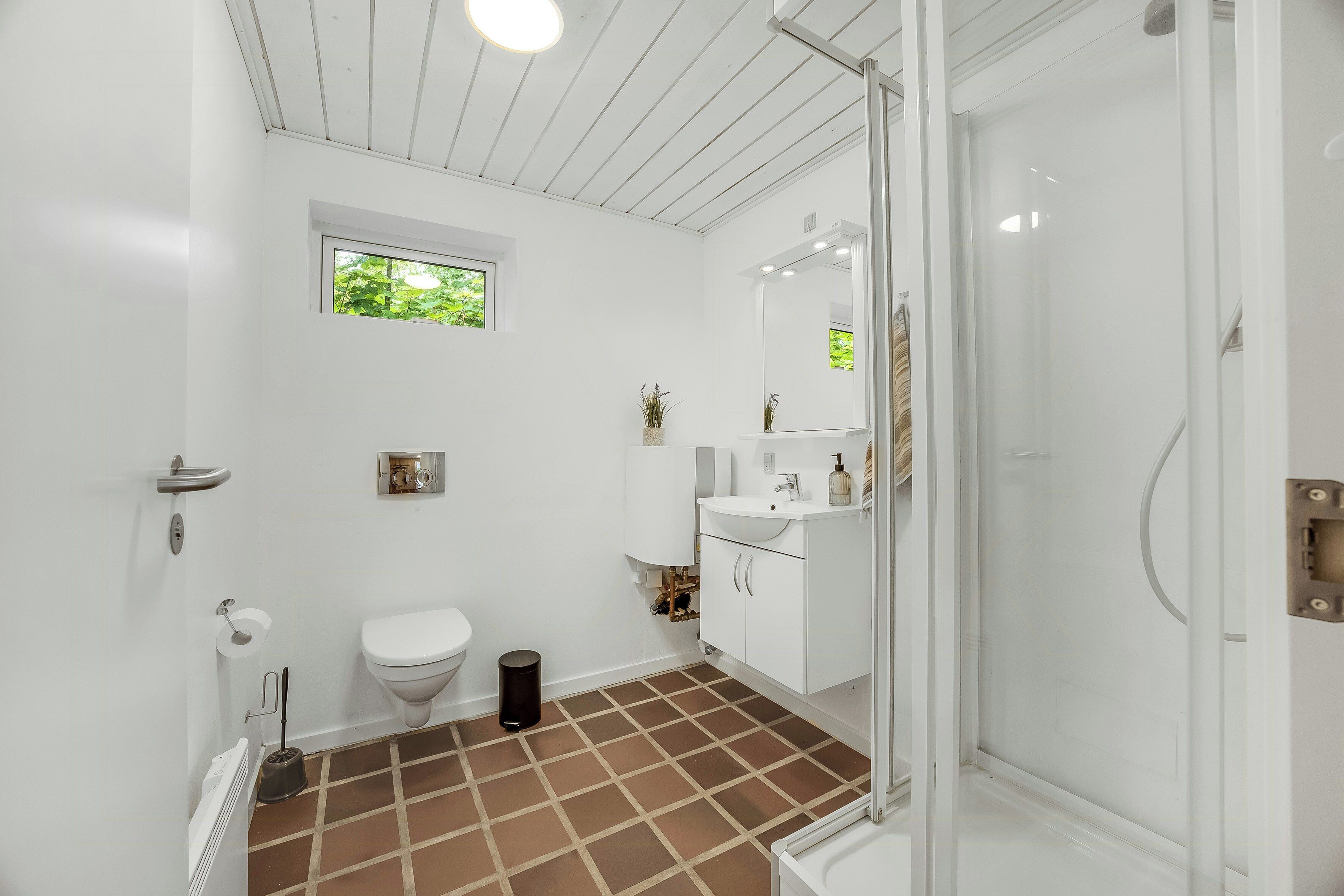 Une salle de bain avec des toilettes blanches, un lavabo, un miroir et un espace douche.
