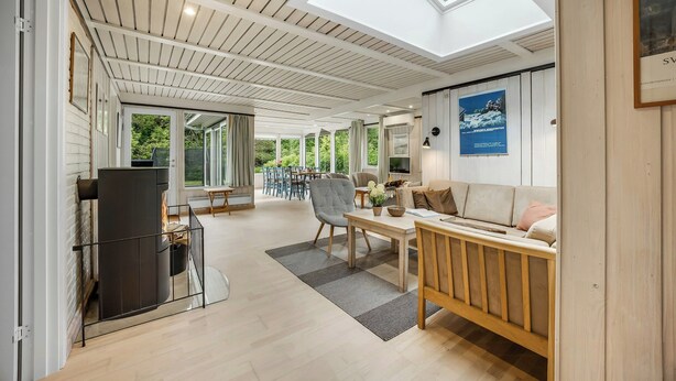 A spacious living area with a high ceiling, a fireplace, a sofa, a dining table, and a view of the outdoors.