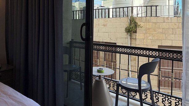 Habitación de hotel con cama, un balcón con mesa y sillas, y vistas a edificios exteriores.
