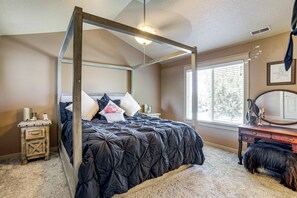 Ein Bett mit Baldachin, ausgestattet mit einer dunklen Steudecke, ein Nachttisch mit Lampe, eine Kommode mit Spiegel und ein Fenster mit Jalousien.