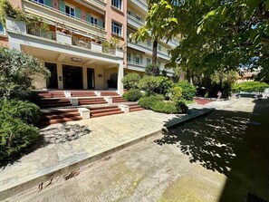 A multi-story building with a covered entrance, steps leading to the entrance, and a courtyard with a water feature. - Ambassador Promenade! (Nice)