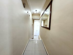 A hallway with a tiled floor, a mirror on the wall, and a door at the end. - 2P Promenade des Anglais LES LIONS HA (Nice)