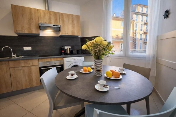 A modern kitchen with wooden cabinets, a built-in oven, and a dining area with a round table and chairs. - 2P Promenade des Anglais LES LIONS HA (Nice)