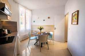 A modern kitchen with a dining area, a built-in oven, and a window with curtains. - 2P Promenade des Anglais LES LIONS HA (Nice)