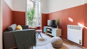 Un salon avec un canapé, un téléviseur et une petite table sur laquelle est posée une plante.