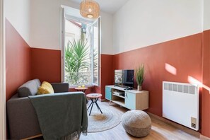 Ein Wohnzimmer mit einer Couch, einem Fernseher und einem kleinen Tisch mit einer Pflanze.