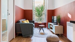 Un espace de vie compact comprenant un canapé, une petite table, un téléviseur et une plante en pot.