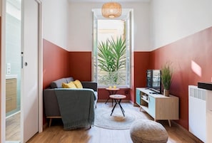 A compact living space with a sofa, a small table, a television, and a potted plant.