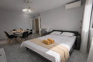 Ein Hotelzimmer mit Bett, Schreibtisch mit Stühlen, einer Hängelampe und einer Klimaanlage.