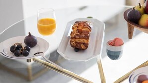 Een tafel met een glas sinaasappelsap, een bord met vijgen en een brood, en een schaal vol fruit.