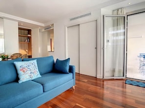 A living room with a blue sofa, a sliding glass door, and a wooden floor. - BLUE RIVIERA TERRACE CENTRAL TRAIN STATION (Nice)