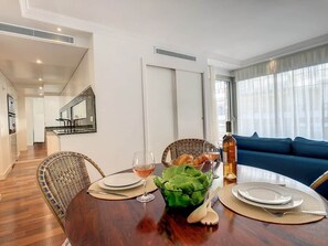 A dining area with a wooden table, wicker chairs, a bowl of salad, wine glasses, and a bottle of wine. - BLUE RIVIERA TERRACE CENTRAL TRAIN STATION (Nice)