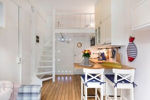 A compact kitchen with a wooden floor, white cabinets, a small dining table with two chairs, a staircase, and a wall-mounted coat rack. - On Board Captain – Studio cosy marin (Nice)