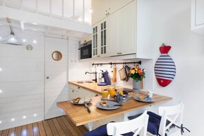 A modern kitchen with white cabinetry, a wooden countertop, and a dining area with white chairs. - On Board Captain – Studio cosy marin (Nice)
