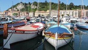 Uma marina com barcos atracados, céu claro e edifícios ao fundo.