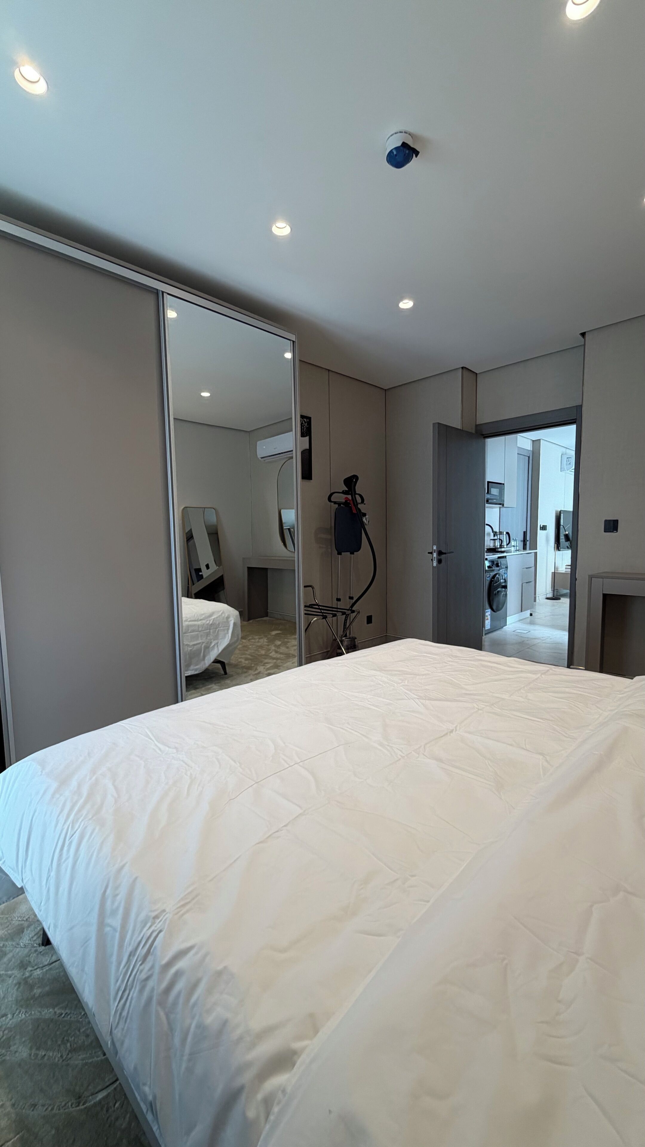 Habitació d'hotel moderna amb un llit gran, un mirall, un aspirador i vista al bany adjacent.