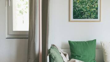 A room with a window, a floor lamp, a sofa with cushions, and a framed painting on the wall.