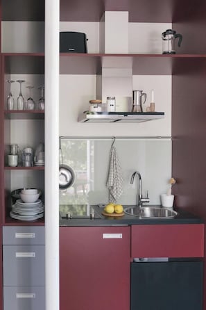 A modern kitchen with a built-in sink, a coffee maker, and a shelf with glassware.