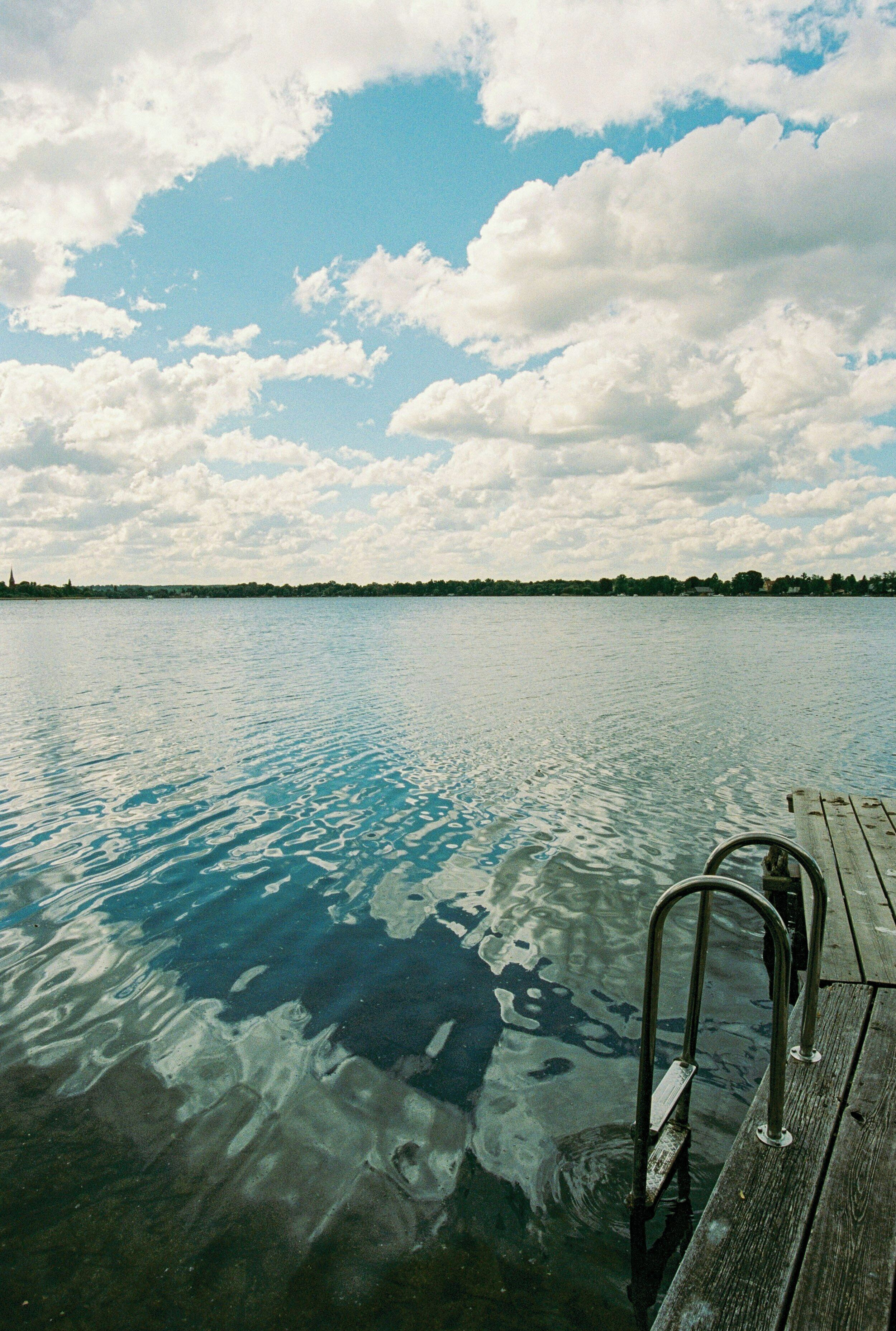 Eine hölzerne Pier erstreckt sich in ein ruhiges Gewässer unter einem wolkenlosen Himmel.