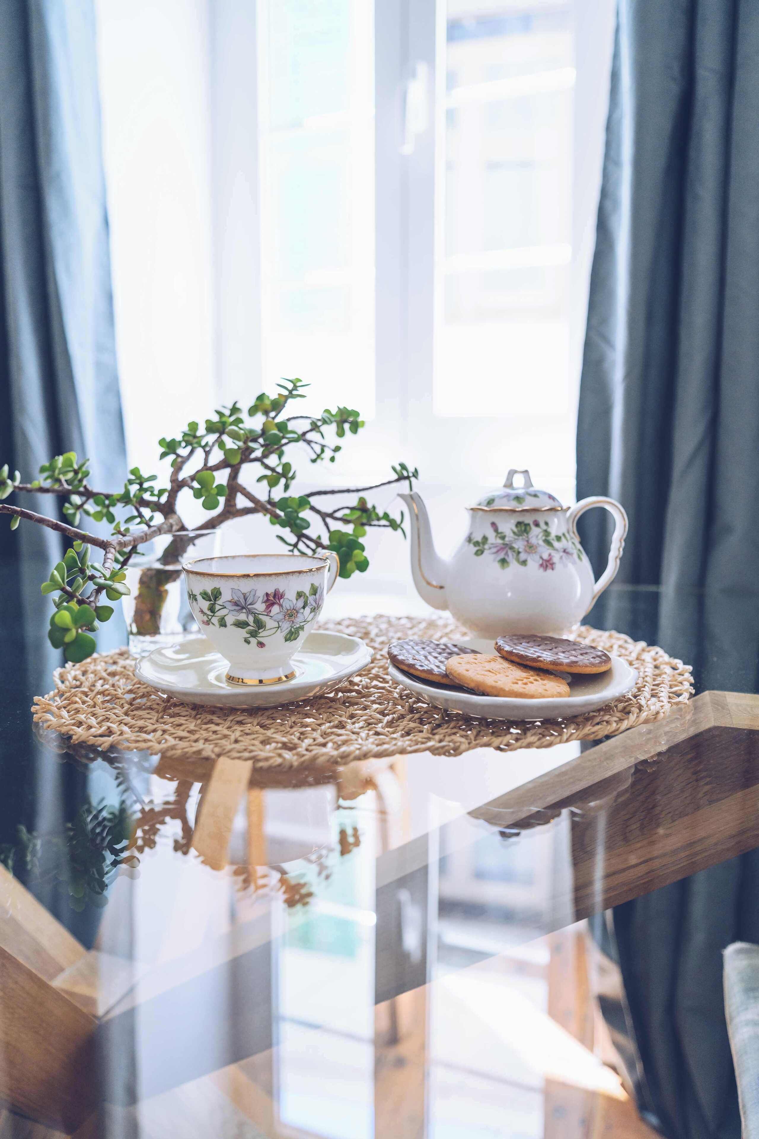 A table with a teapot, cup, and cookies on a placemat.