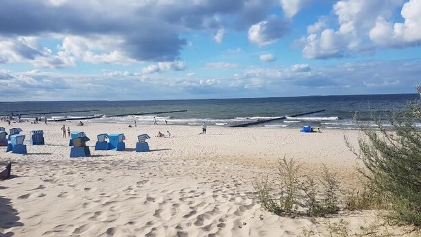 Uma praia com areia, algumas pessoas e algumas estruturas azuis.