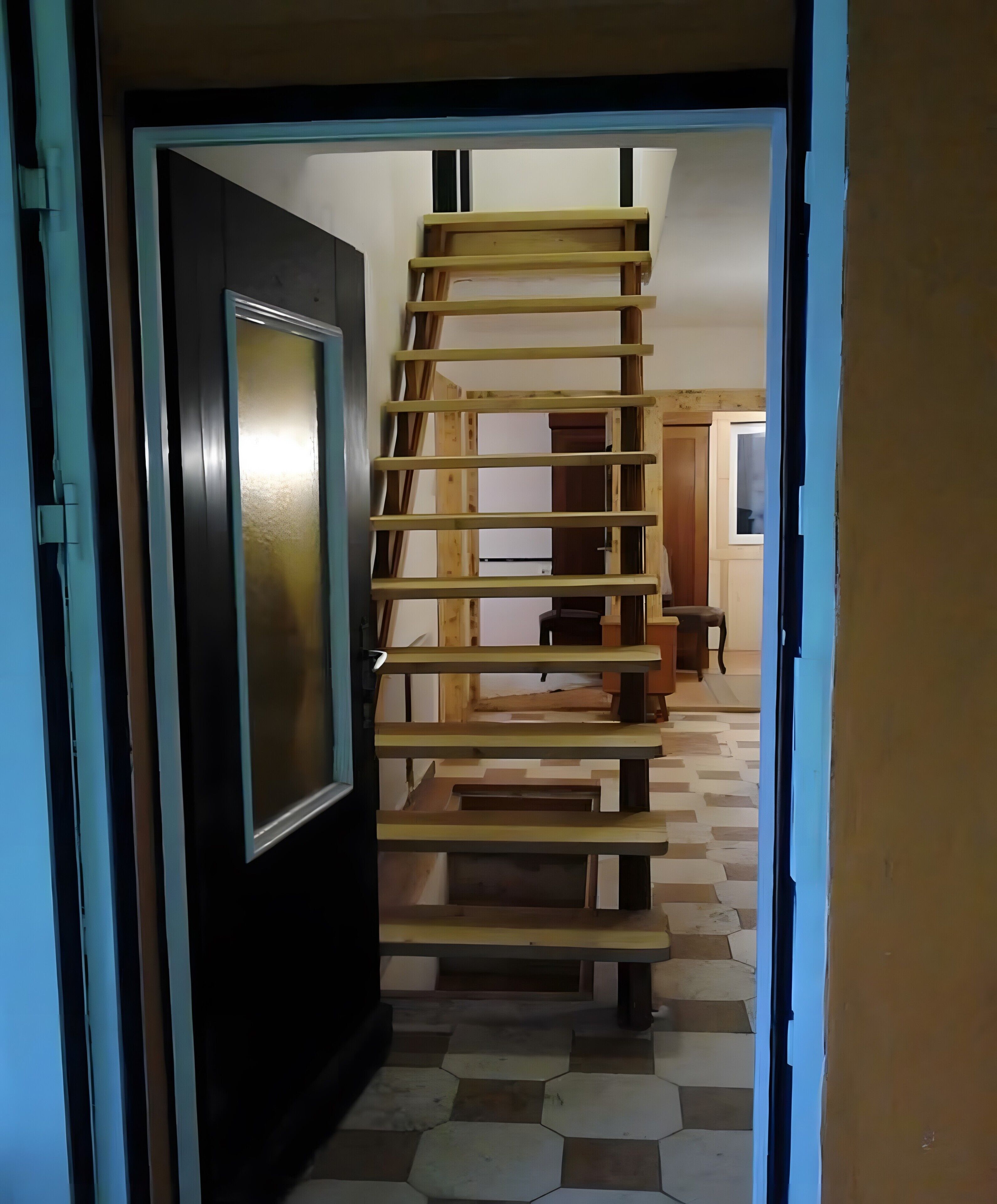Un pasillo con una estructura de escalera de madera, una puerta y un piso de baldosas.