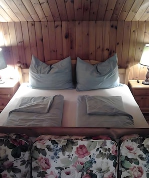 A wooden-paneled room with a bed, two pillows, a nightstand, and a lamp. - Mountain Hut 'Chalet Adlerhorst Am Großglockner' with Mountain View, Private Terrace and Private Garden (Wolkersdorf)