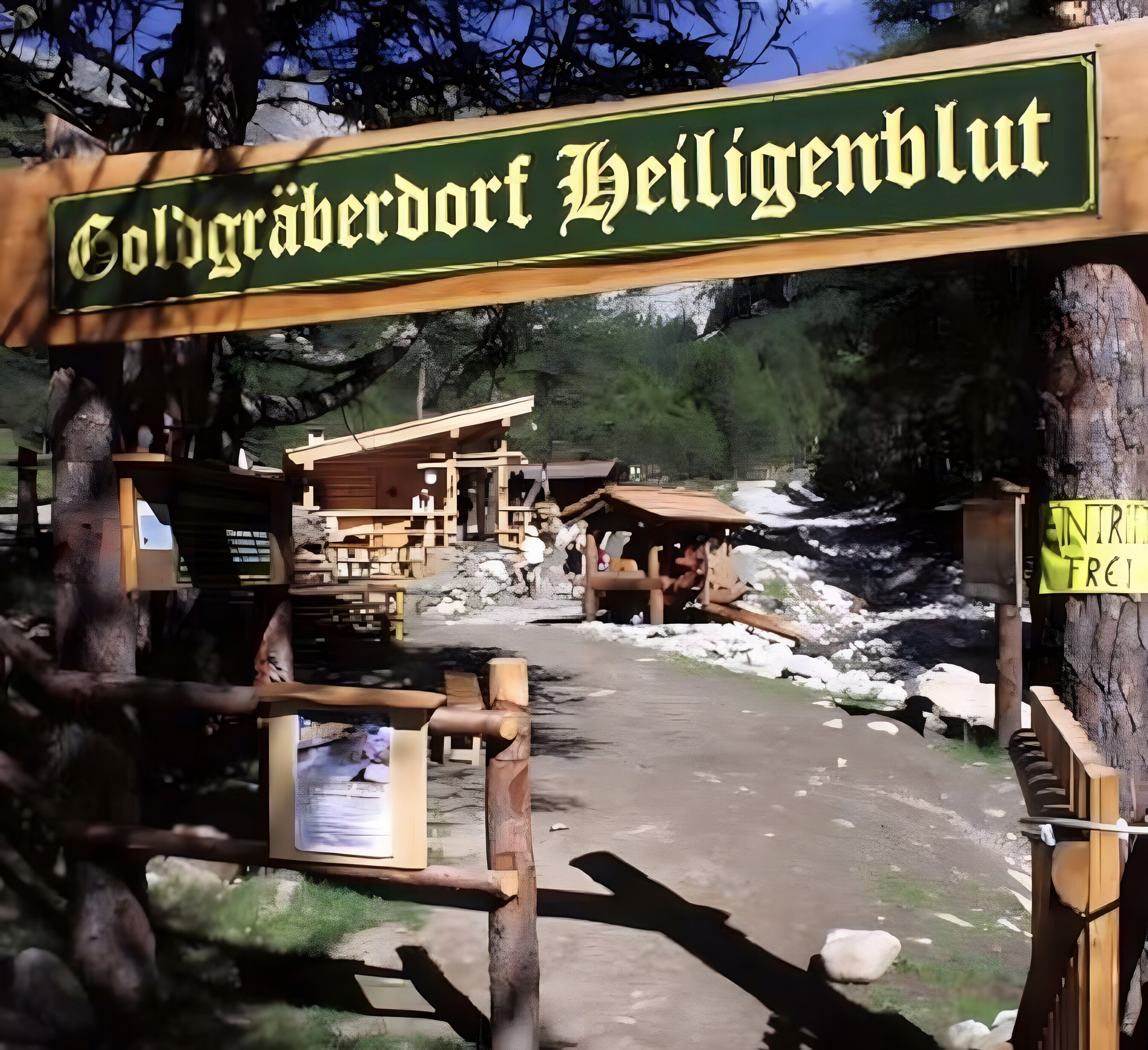 Een houten bord met de tekst 'Coldgärberdorf Heiligblut', een houten hut en een pad dat naar een berglandschap leidt.