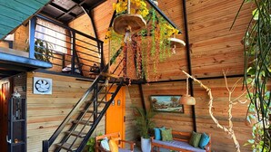A rustic wooden interior with a staircase, wooden furniture, and hanging plants.
