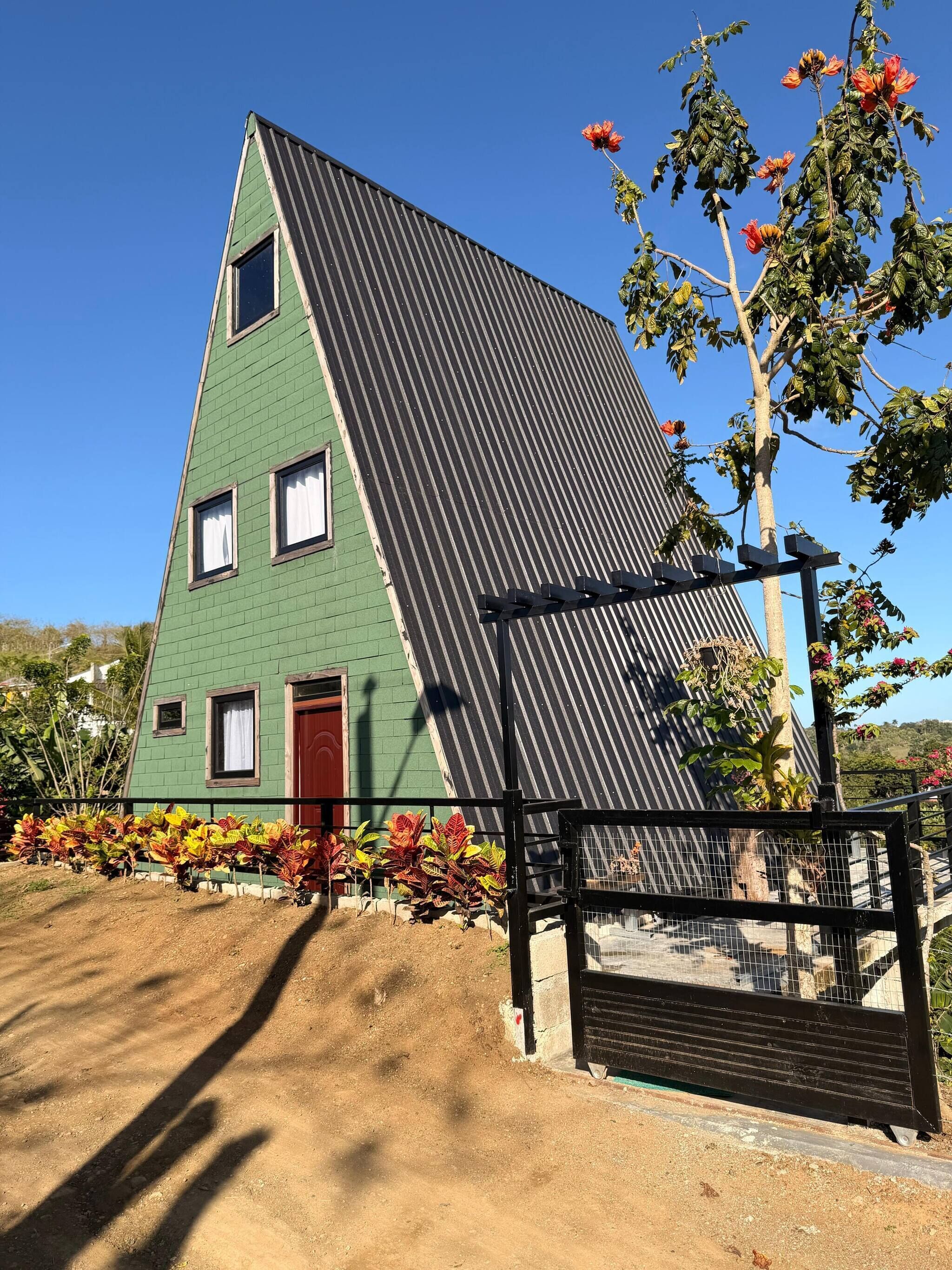 Een gebouw met een groen dak, een driehoekige vorm, een rode deur en een zwart hek.