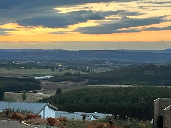 Un paisaje rural con una casa y una edificación pequeña al frente, rodeado de árboles y campos abiertos.