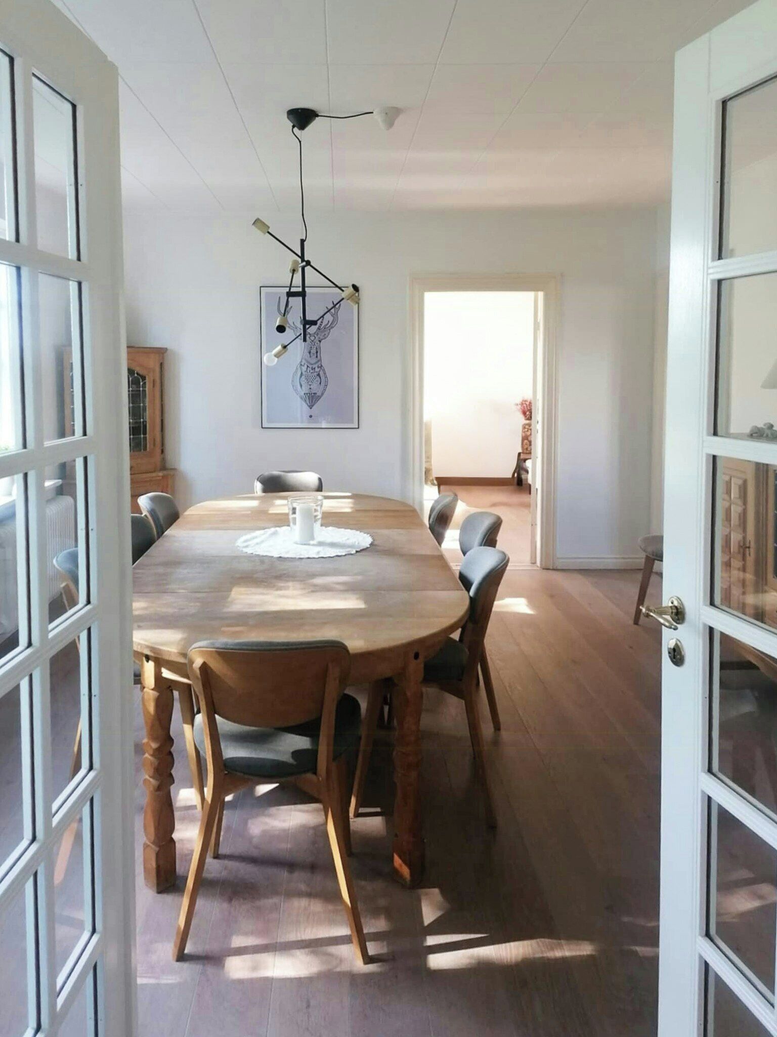 Un comedor con una mesa de madera, sillas, una lámpara colgante y una obra de arte enmarcada en la pared.