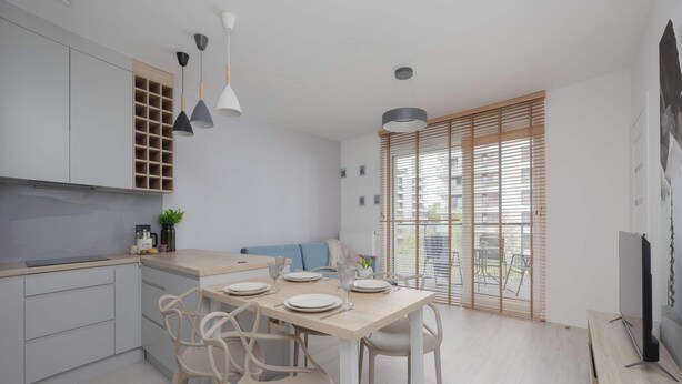 Eine moderne Küche mit weißen Schränken, einem Esstisch für vier Personen und einem großen Fenster mit Jalousien.